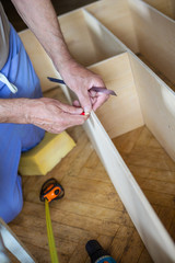 Mature man measuring wooden shelf with measure tape and making marks with pencil