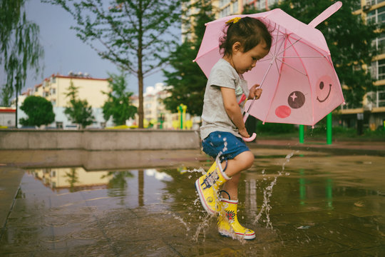 Baby girl Girl wearing rubber boots and jumping in rain puddle