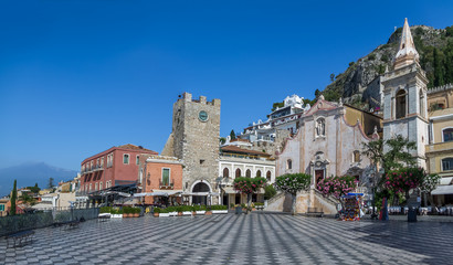 Panoramic view of Taormina main square (Piazza IX Aprile) with San Giuseppe Church, the Clock Tower and Mount Etna Volcano on background - Taormina, Sicily, Italy