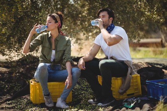 Couple drinking water while sitting on crates