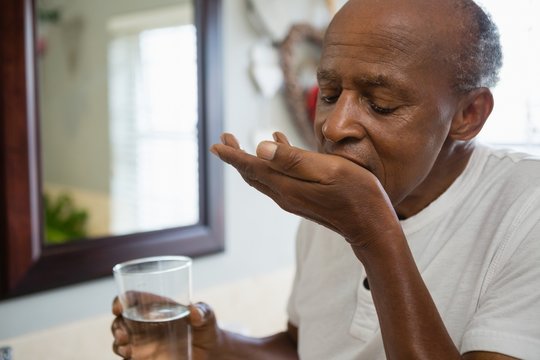 Senior Man Taking Medicine In Bathroom