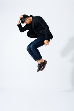 Asian man wearing black suit jumping over white background 