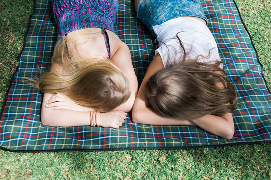 Looking down on two teenage girls lying face down on a picnic rug 