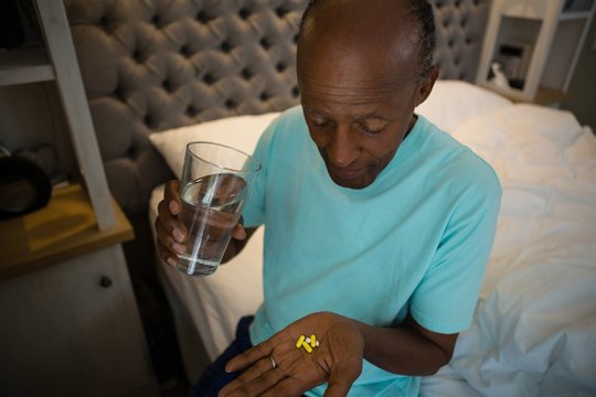 Senior man taking medicine while sitting in bedroom