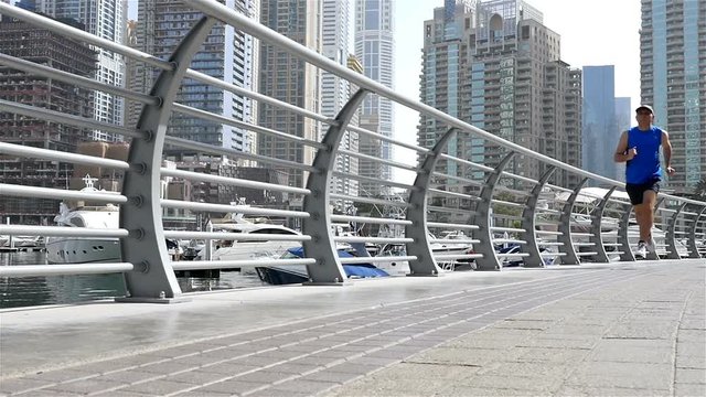 Low angle view of athletic fitness man running jogging in Dubai Marina in the morning, slow motion