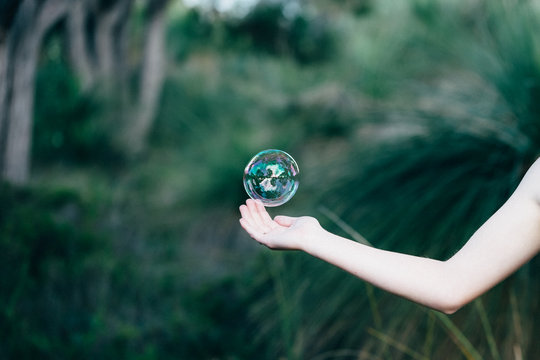 Girls hand reaching out catch a bubble in the bush