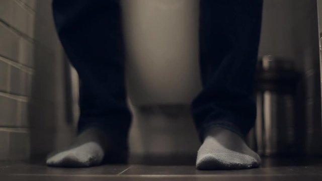 The man takes off his pants in the toilet and sits down on the toilet, he pulls up his pants and leaves