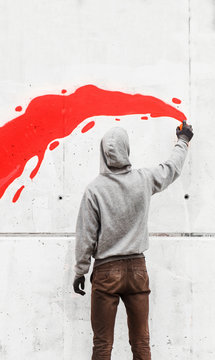 Street artist drawing red splash with spraycan on wall