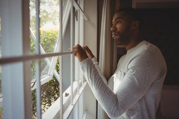 Thoughtful man looking out through window at home