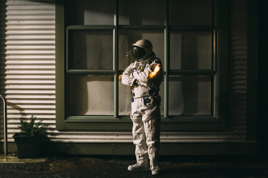 A spaceman stands tall and proud outside a house at night 