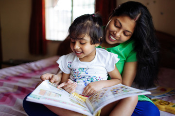 Little girl reading a book sitting on her mother's lap