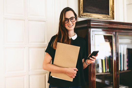 Young businesswoman holding a folder and smart phone in a workplace 