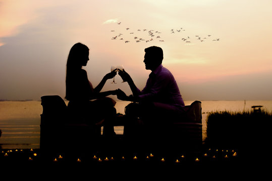 silhouette romantic couple enjoying glass of wine in a beautiful sunset at the rim of beach