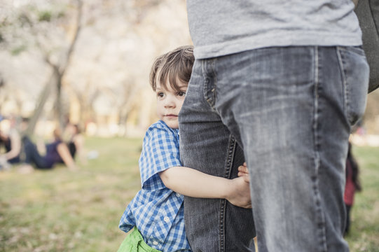 Little Boy Holding Onto His Father's Leg While At The Park