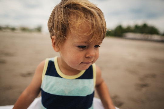Funny toddler boy acting grumpy on beach wearing tank top