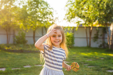 cute little girl eating a lollipop on the grass in summertime.