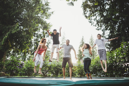 Candid moment of happy family with teenagers playing on trampoline