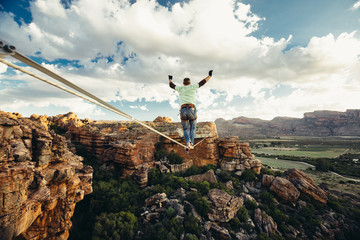 Man balance walking on a highline or tight rope high over a mountain valley at sunset