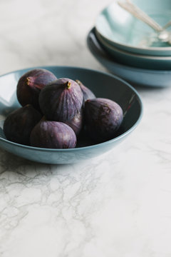 Ripe seasonal figs in a blue bowl on a marble surface