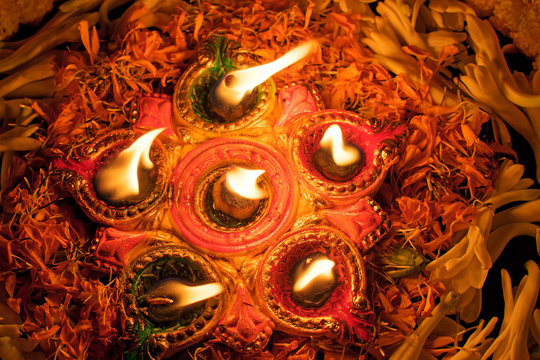 Top view of Rangoli flowers put in circle and candles or diyas placed around them, Deepawali lights at night. Dark background stock image.