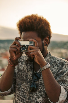 Young black man taking a photo with an old camera at sunset