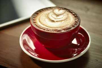 Red cup of cappuccino with beautiful latte art on old wooden background