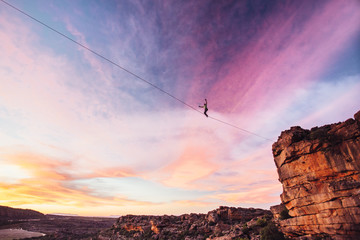 Man balance walking a highline or tight rope high over a rocky valley at sunset