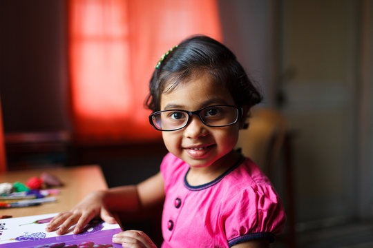 Cute little girl with glasses holding an open book on table and smiling