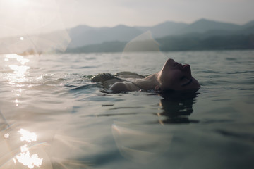 Young woman floating in lake at sunset