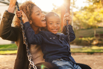Black mother and her son having fun on playground swing