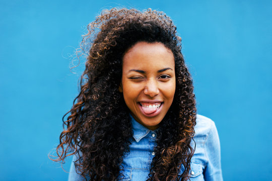 Young african woman sticking her tongue in front of a blue wall