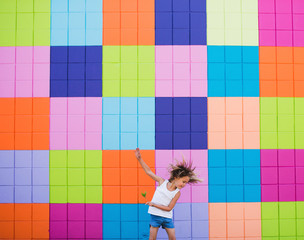 Cute young girl having fun dancing near colorful wall in summer