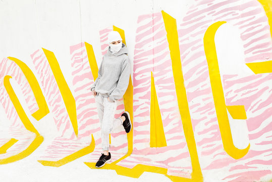 Hip and trendy female with balaclava mask over face standing in front of "SWAG" graffiti