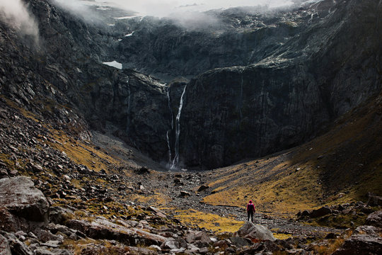 A young traveler stares at the ominous waterfall and mountain ahead of her 
