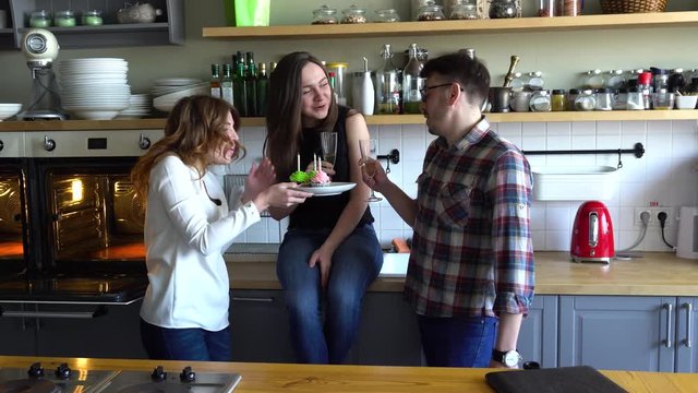 two girls and guy blow out candles on the cupcake at the kitchen on muffine