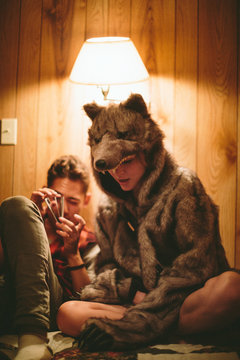 A boy and girl in a wolf costume sit on a bed together as he reads and she listens