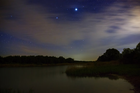 Bright stars in the night sky with clouds on a background of the river.