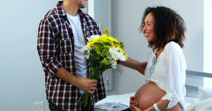Man offering bunch of flowers to his pregnant woman in ward