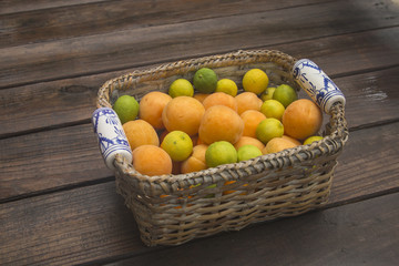 Obraz na płótnie Canvas Apricot, oranges and limes in wicker basket with ceramic hand painted handles 