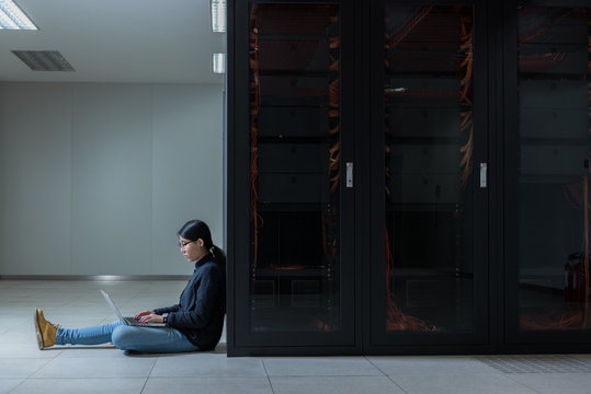 Side view of technician working on laptop in data center - Powered by Adobe