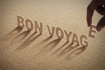 BON VOYAGE wood word on compressed or corkboard with human's finger at E letter.