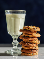 Glass of milk and cookies on stone table with dark wall background