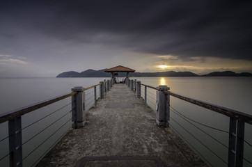 Long exposure jetty during sunset with dramatic clouds and golden light