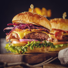 Delicious fresh burger with meat, bacon, cheese and vegetables on a wooden board, in a rustic soul...