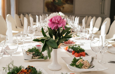 Beautiful wedding bouquet of white and pink peonies in white vase on dinner table in blur. Table setting at luxury wedding reception. Flowers on the table