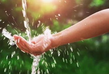 Fotobehang Water gietende plons in de hand en natuur achtergrond met zonneschijn © lovelyday12