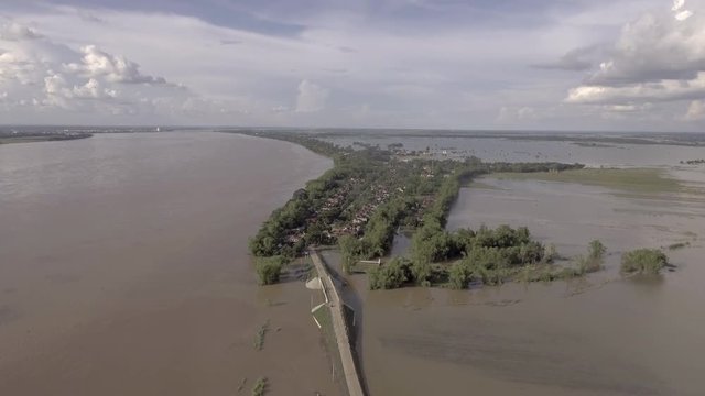 Drone shot: worst flooding ravaging Southeast Asia, drowning the agricultural land. A bridge running across the flooded river in the foreground