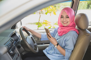 beautiful woman wearing hijab holding a smartphone while driving