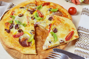 Home made pizza with smoked sausage, olives, tomates, cheese and basil on a olive wood cutting board