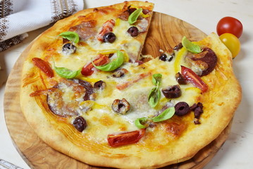 Home made pizza with smoked sausage, olives, tomates, cheese and basil on a olive wood cutting board